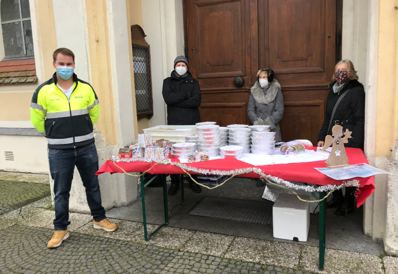 Helfer der Caritas stehen vor der Kirche Sankt Magdalena in Fürstenfeldbruck an einem Tisch mit verpacktem Weihnachtsessen.