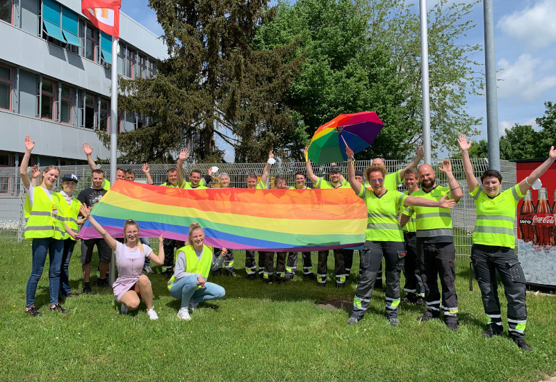 Verschiedene Mitarbeiter von Coca-Cola hissen gemeinsam die Regenbogenflagge am Standort Fürstenfeldbruck. 