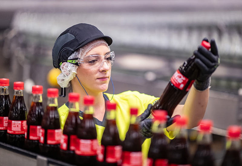Produktionsmitarbeitende kontrolliert Coca-Cola Flaschen