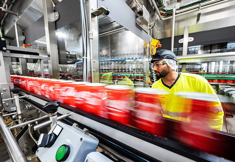Mitarbeiter kontrolliert Coca-Cola Dosen auf Fließband