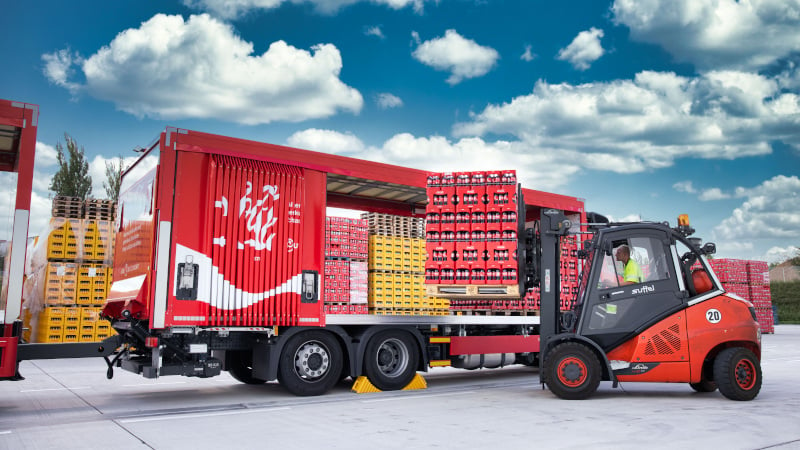 Ein Gabelstapler belädt einen LKW der „Roten Flotte“ von Coca-Cola mit Getränkekisten.