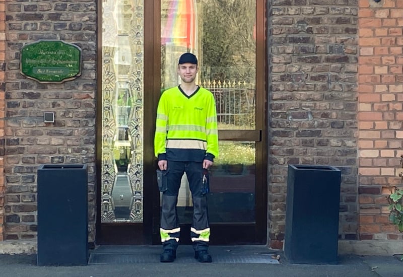 Produktionsmitarbeiter Niklas Flier steht in Arbeitskleidung vor dem Gebäude des Coca-Cola Standorts Bad Neuenahr-Ahrweiler.