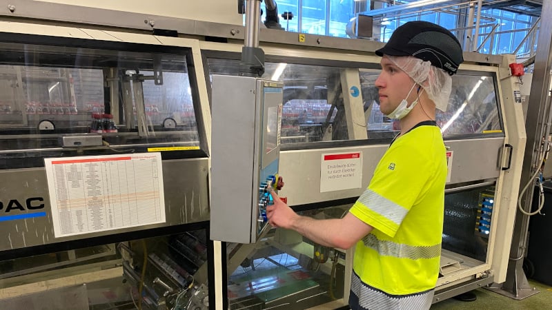 Der Coca-Cola Mitarbeitende Niklas Flier bei der Arbeit. Er bedient konzentriert eine Maschine in der Produktion des Werkes Bad Neuenahr-Ahrweiler. 