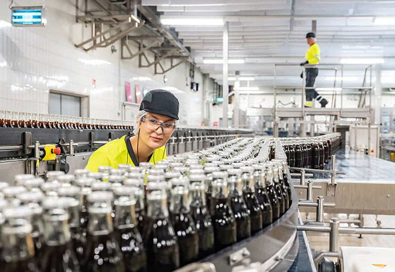 Mitarbeiterin prüft Coca-Cola light gefüllten Glasflasche